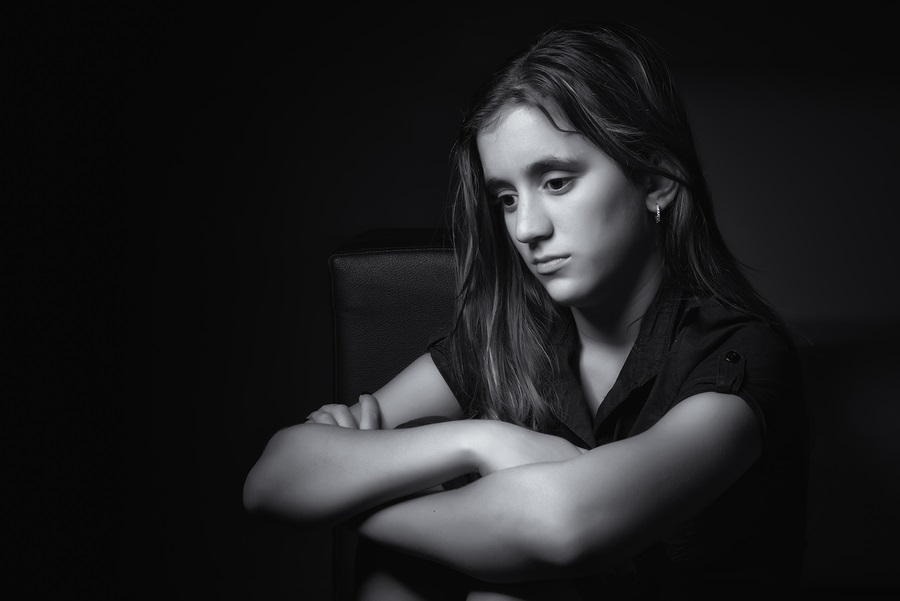 Black and white low key portrait of a sad teenage girl with a thoughtful and worried expression